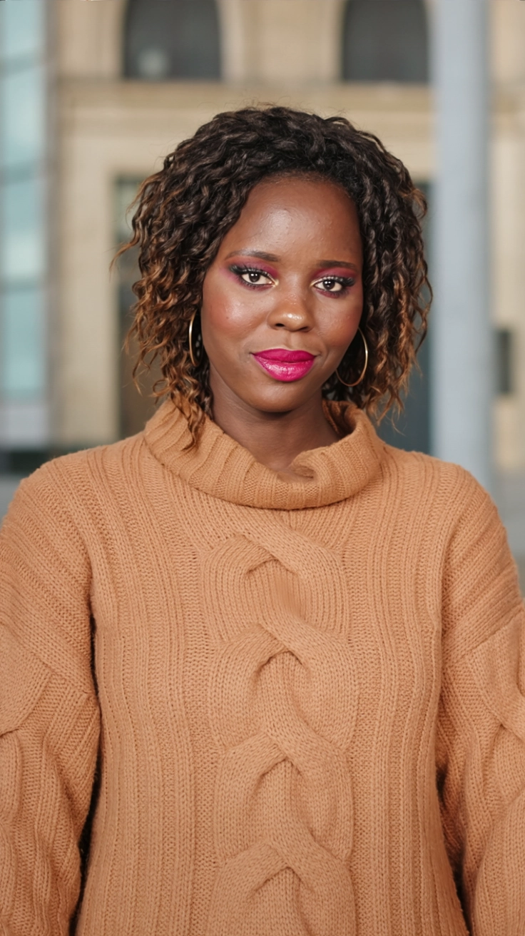 A close-up of a woman wearing a chunky knit sweater with a high collar in burnt orange