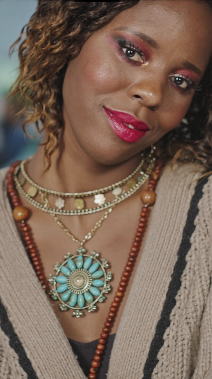 A close-up of a young woman wearing layered statement jewelry, including bold necklaces and earrings, styled with a cozy winter outfit.