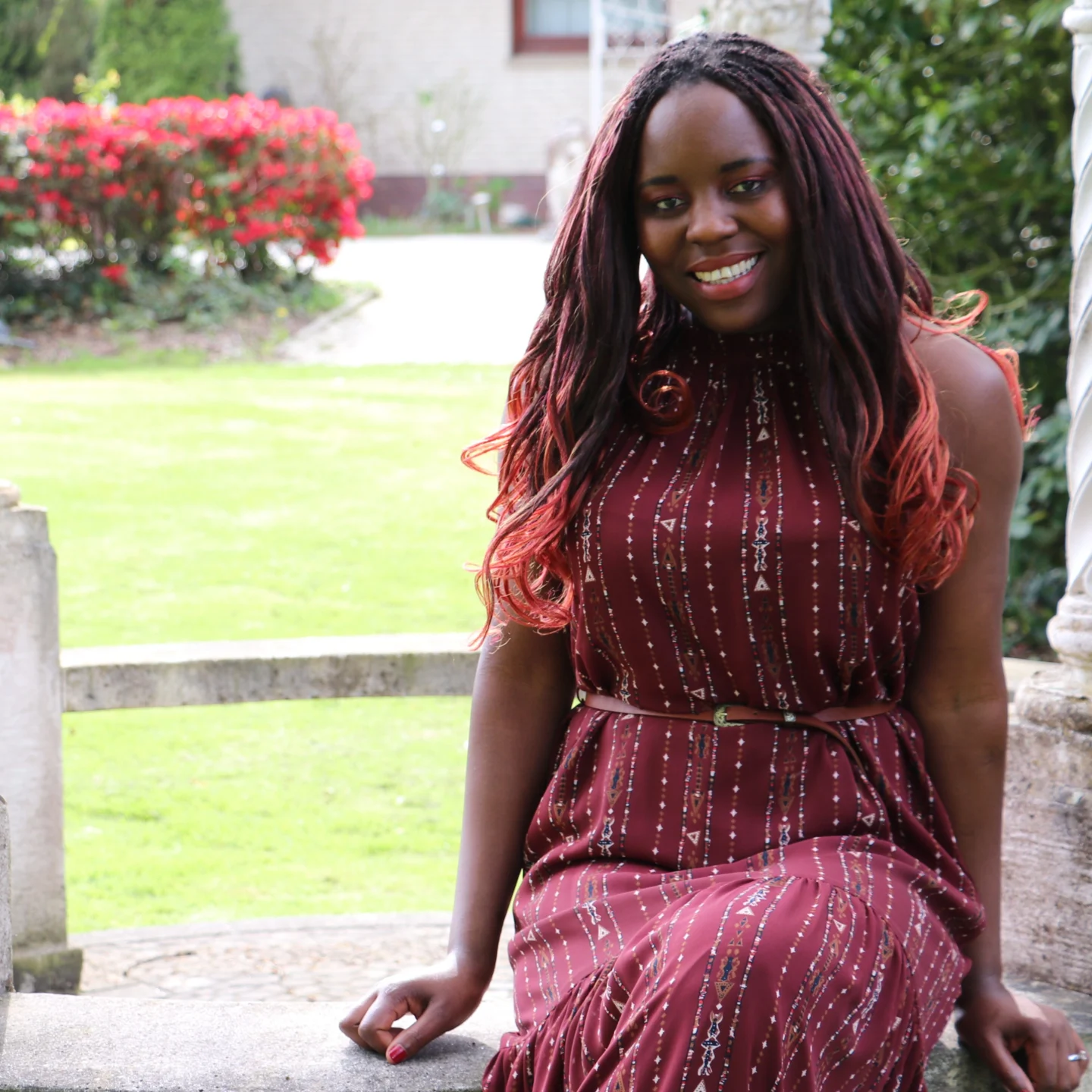 A photo of me in spring wearing a red maxi dress with white dots. Sitting.
