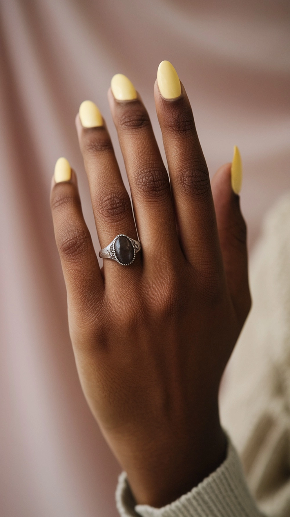 How to Style Butter Yellow Nails for a Radiant Look 2 A hand with butter yellow nails and a silver ring on a light background.