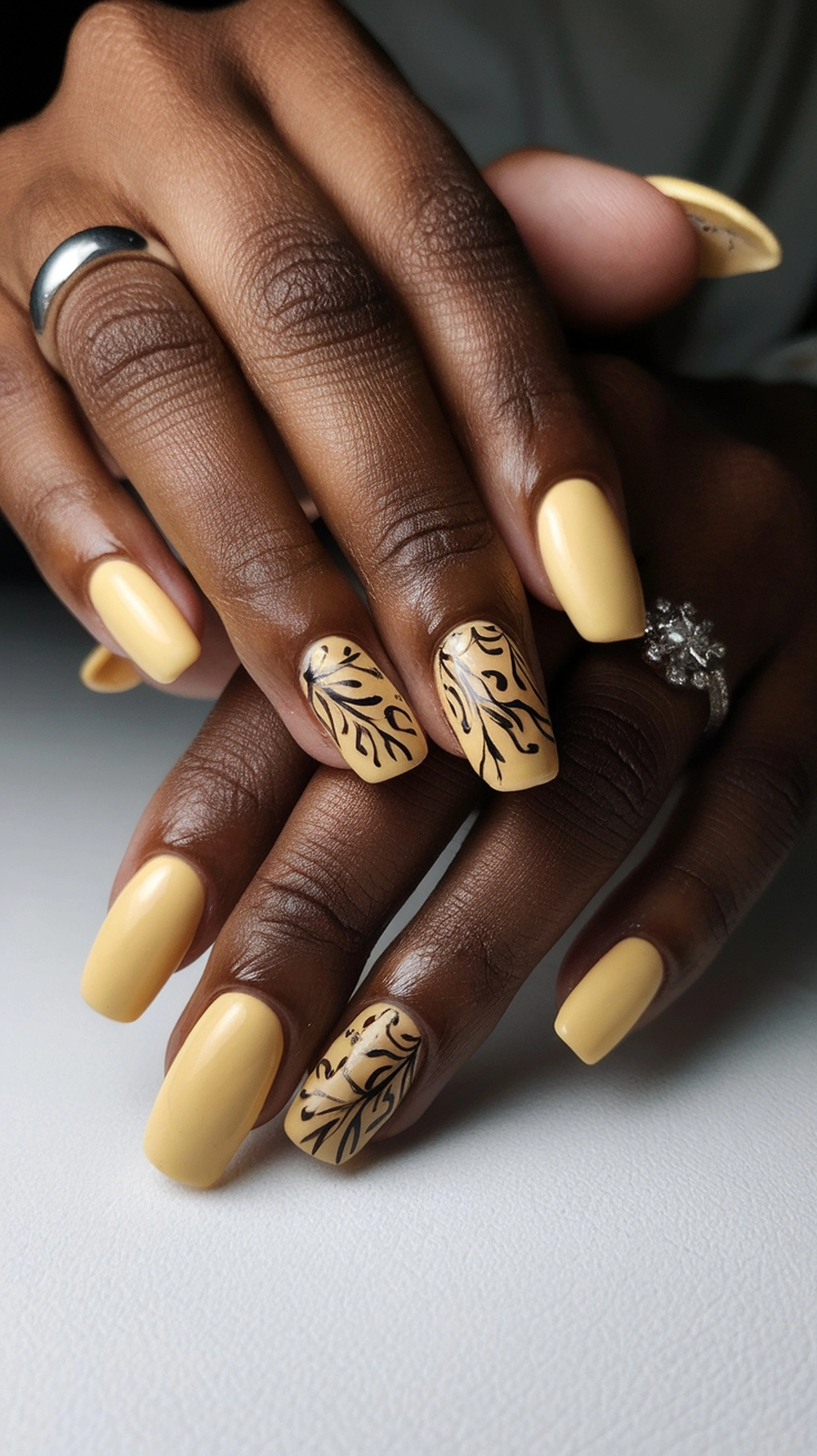 Close-up of beautifully manicured butter yellow nails with intricate black designs