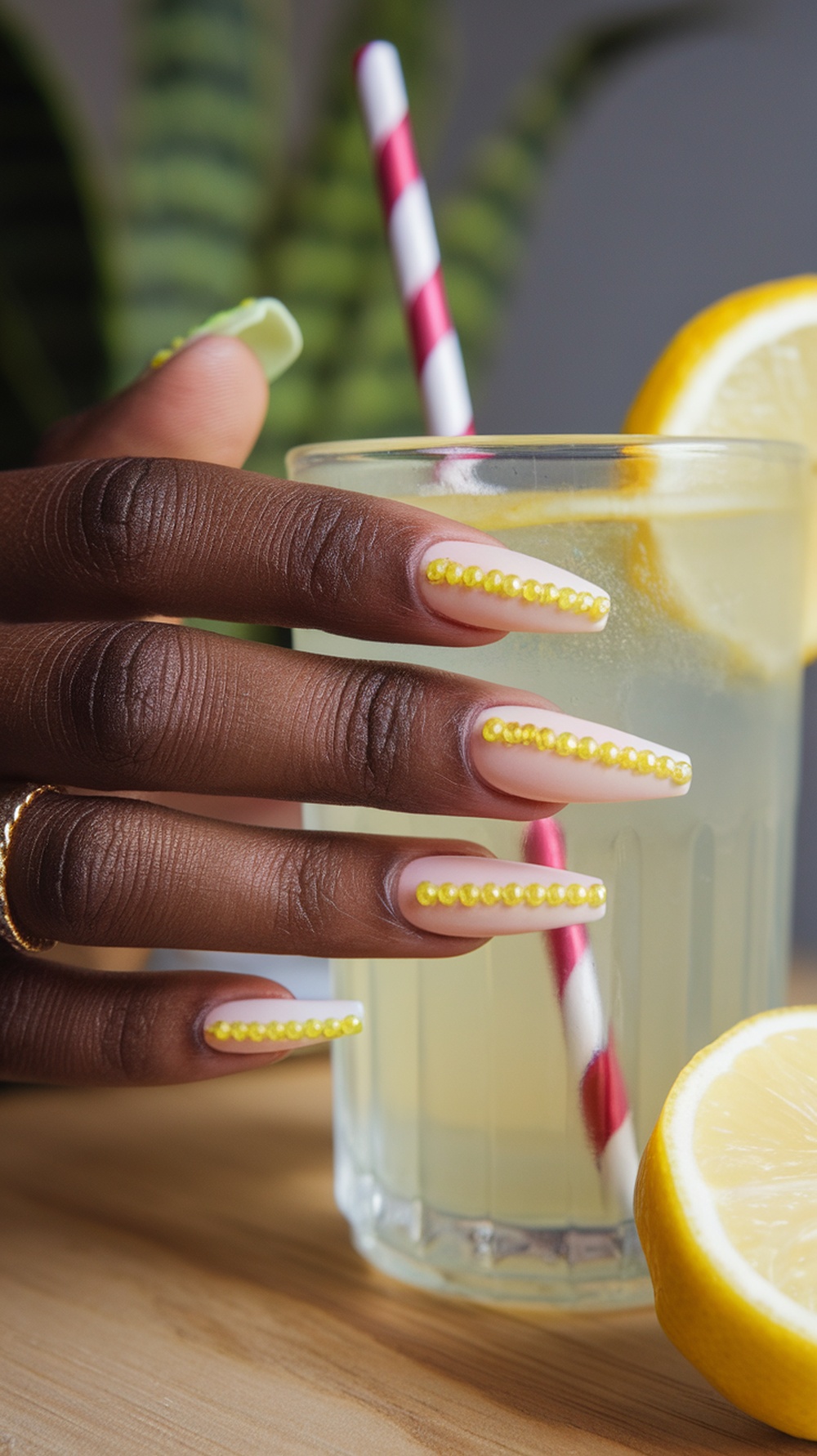 Lemonade-inspired nails with yellow beads on a nude base, next to a glass of lemonade.