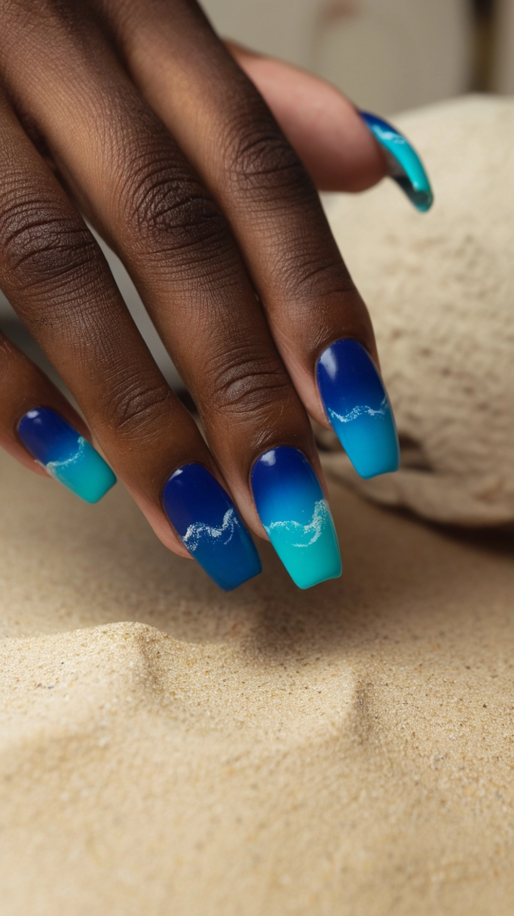 Close-up of a hand with ocean wave ombre nails in blue and turquoise shades.