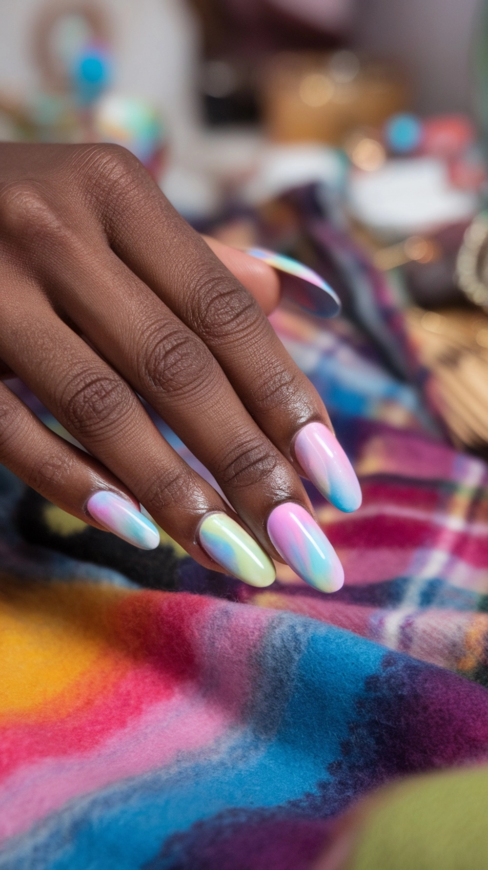 16 Cute Boho Nail Ideas You’ll Love 15 A close-up of a hand with colorful tie-dye effect nails resting on a vibrant fabric.