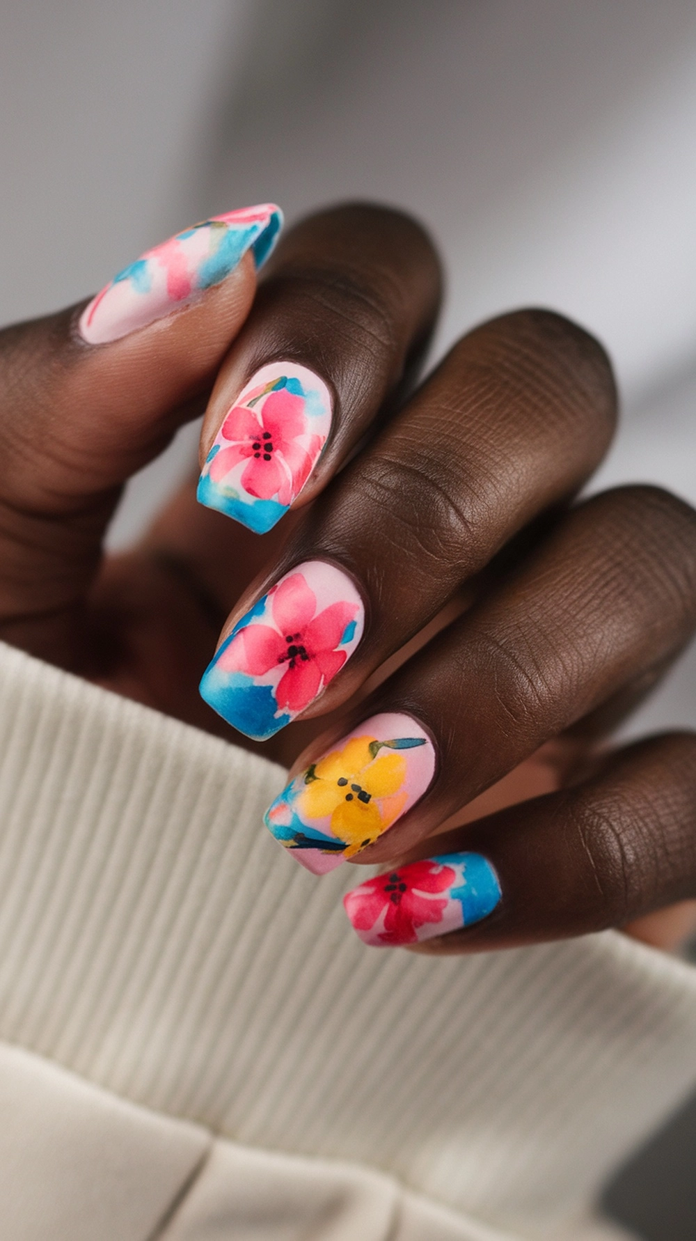 16 Cute Boho Nail Ideas You’ll Love 13 Close-up of colorful floral watercolor nails with pink, yellow, and blue designs on a hand.