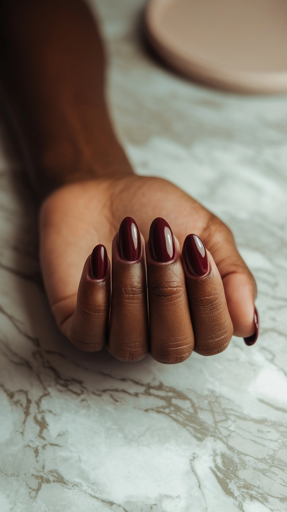 How to Style Burgundy Nail Designs for a Bold Stunning Look 2 A hand displaying elegant burgundy nails on a marble surface.