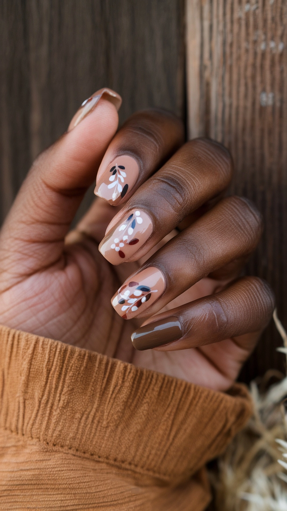 16 Cute Boho Nail Ideas You’ll Love 7 Close-up of a hand with earthy toned nails featuring floral designs, resting on a textured fabric.