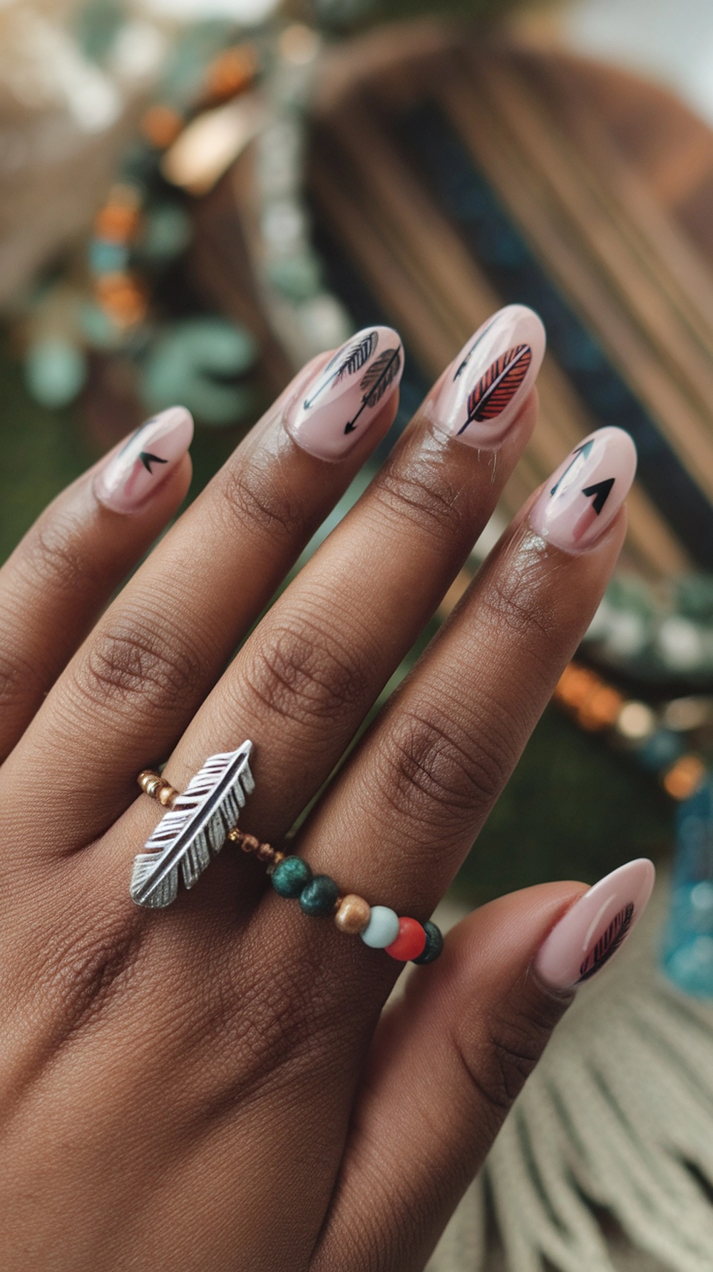 16 Cute Boho Nail Ideas You’ll Love 9 Close-up of hands with feather and arrow nail art on a soft pink background, showcasing boho chic style.