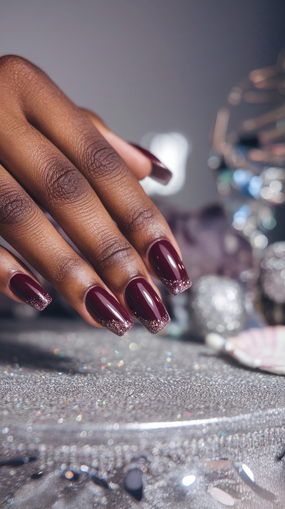 How to Style Burgundy Nail Designs for a Bold Stunning Look 8 A close-up of a hand with burgundy nails featuring glittery tips, showcasing a stylish nail design.
