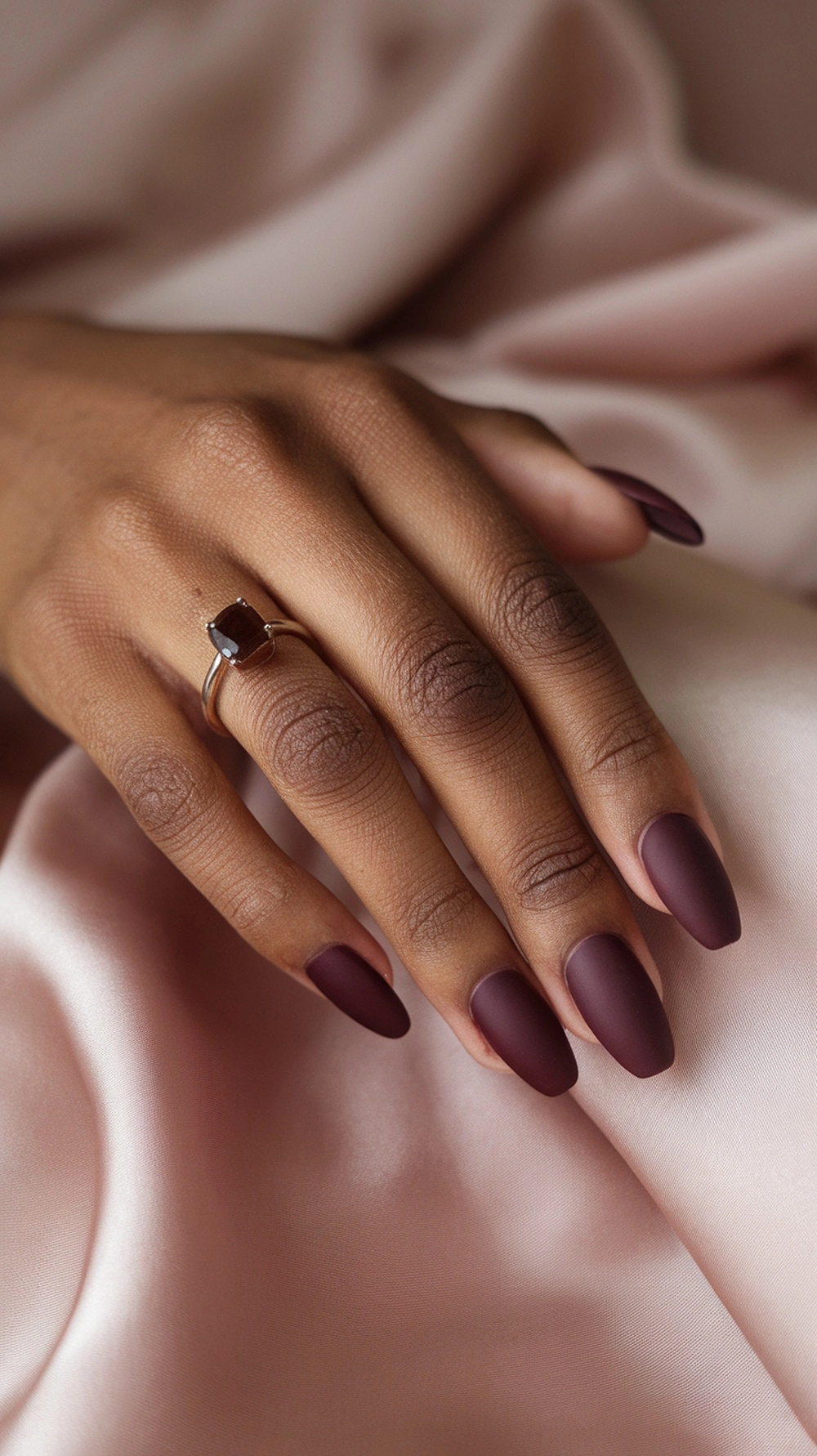 How to Style Burgundy Nail Designs for a Bold Stunning Look 9 A close-up of matte burgundy nails on a hand, resting on a soft fabric background.