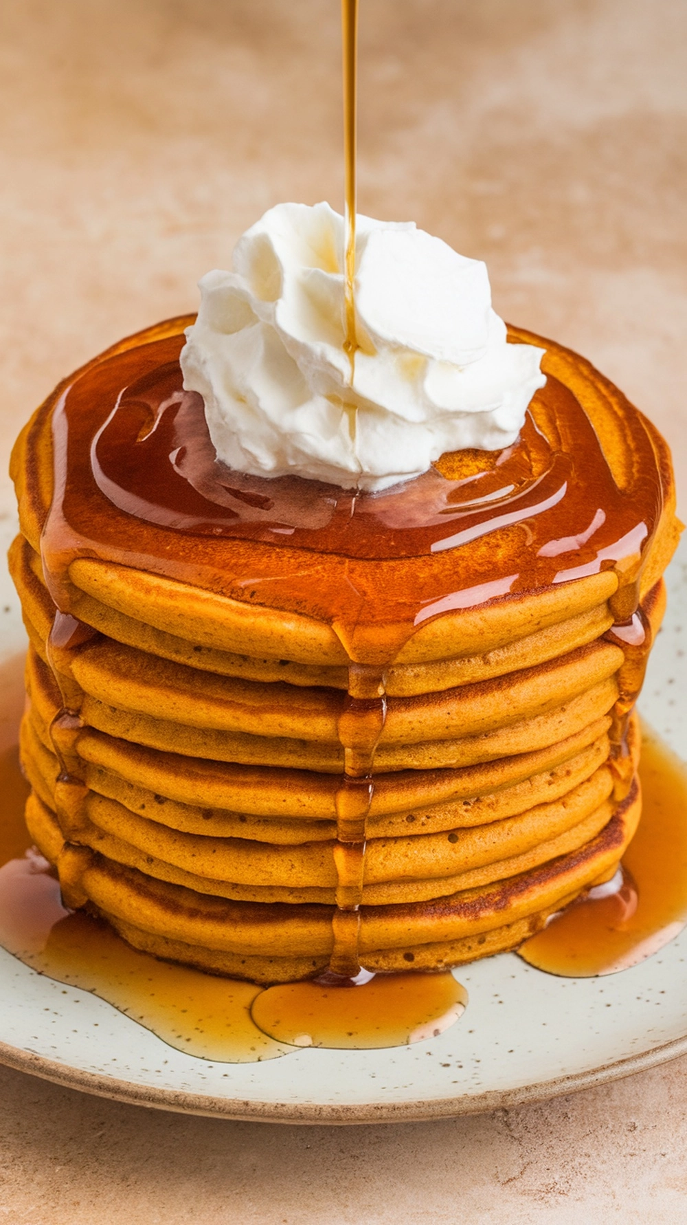 A stack of fluffy pumpkin pancakes topped with whipped cream and maple syrup.