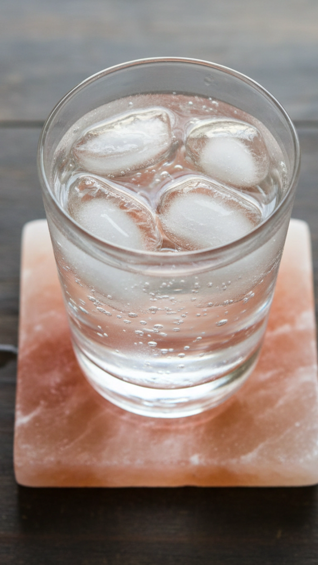 Overhead view of a drink glass resting on a small, polished square coaster made of natural Himalayan salt.