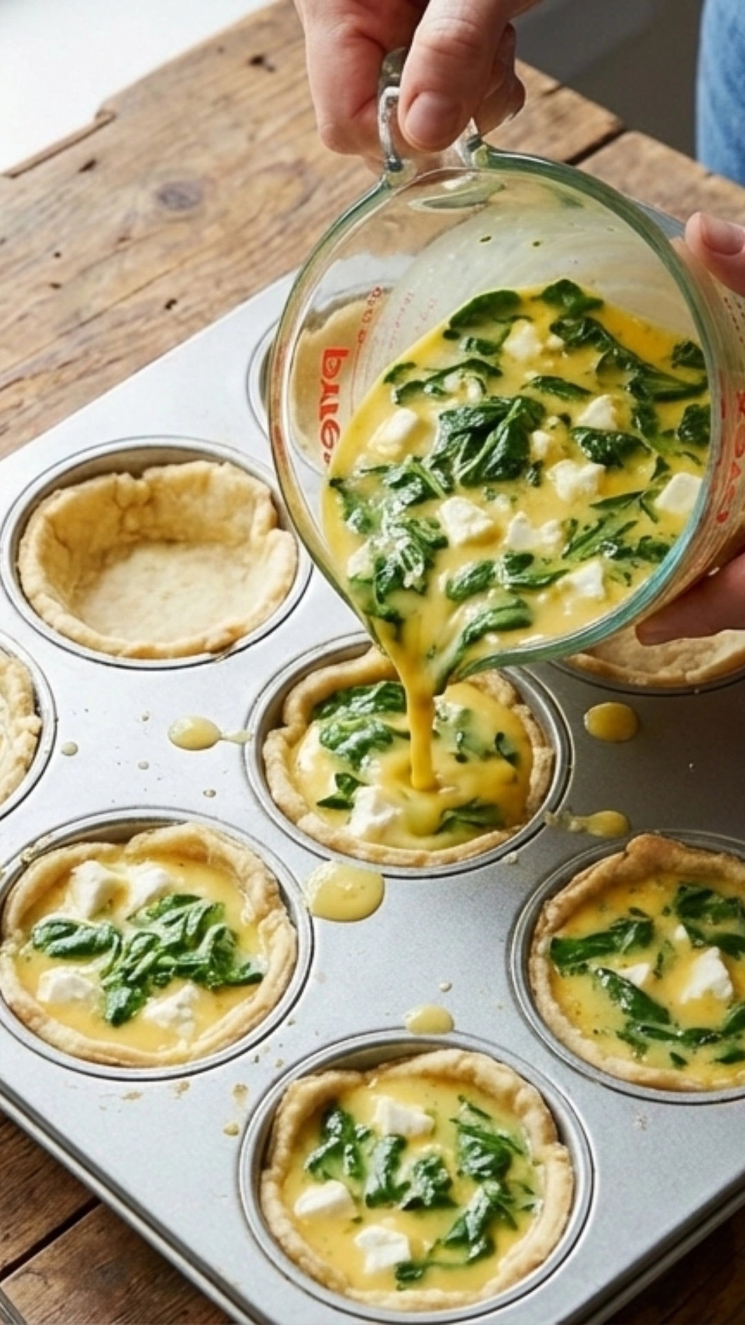 Easy Mini Quiches with Spinach and Feta 3 Pouring egg custard into mini quiche crusts in muffin tin.