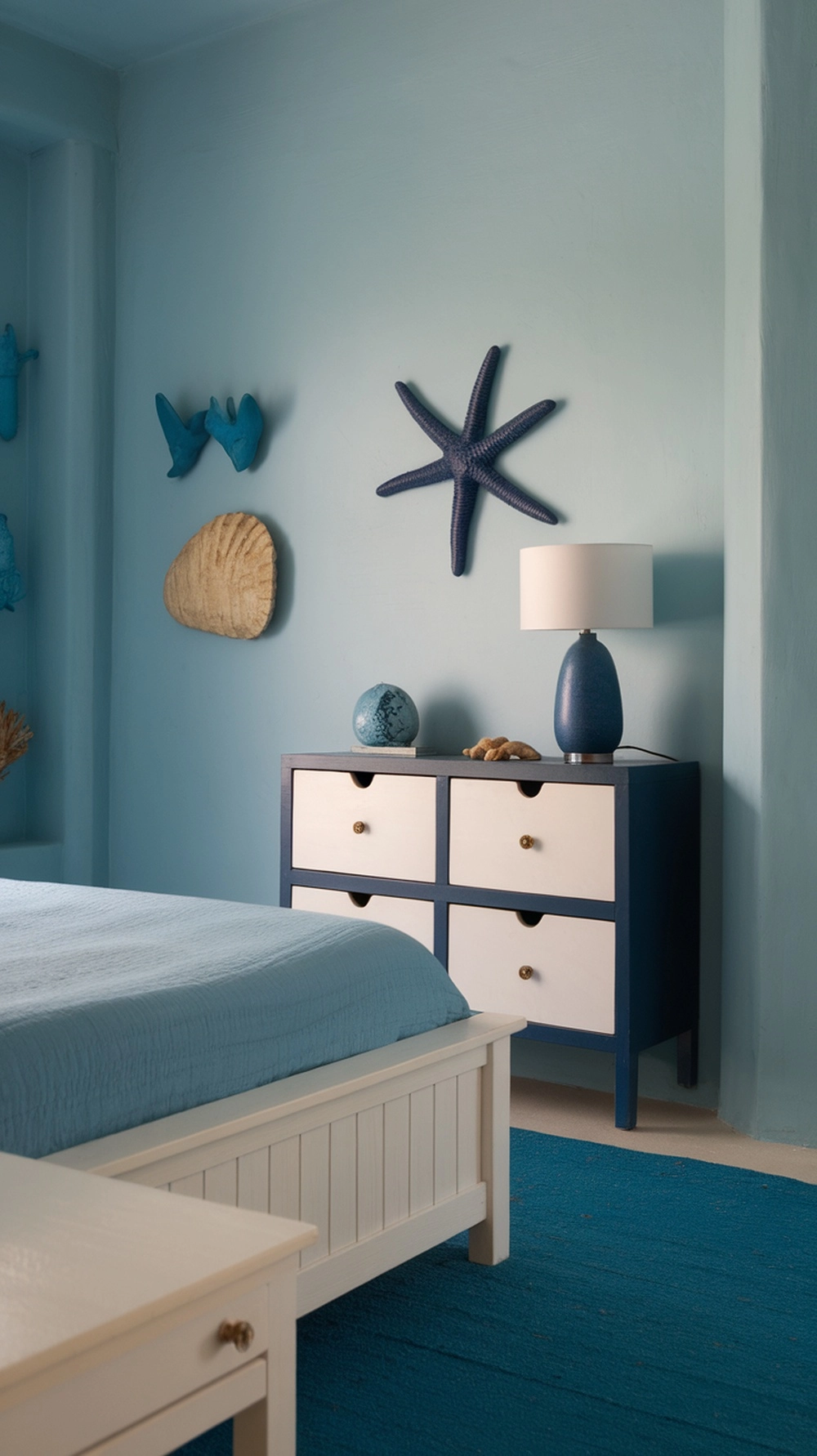 A serene bedroom with light blue walls, white furniture, and ocean-themed decor.