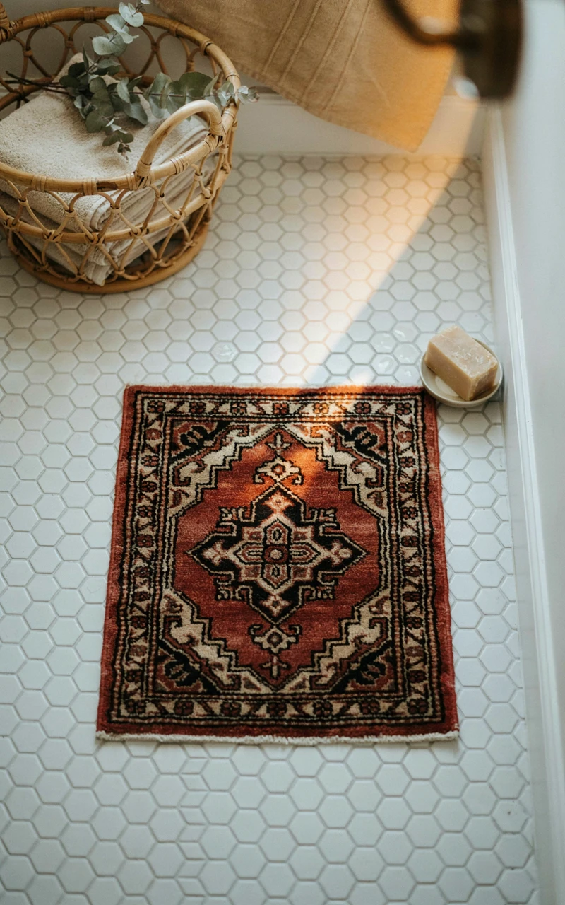 21 Cozy Bathroom Ideas for Fall That Feel Warm and Inviting 4 A faded red and brown vintage-style rug on a white tile bathroom floor.