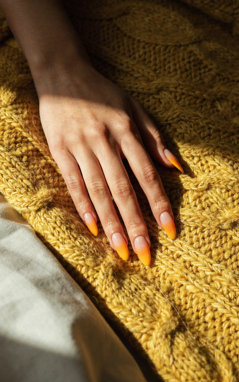 A dark brown woman's hand on a yellow blanket showing long coffin nails with a white, orange, and yellow candy corn ombre.