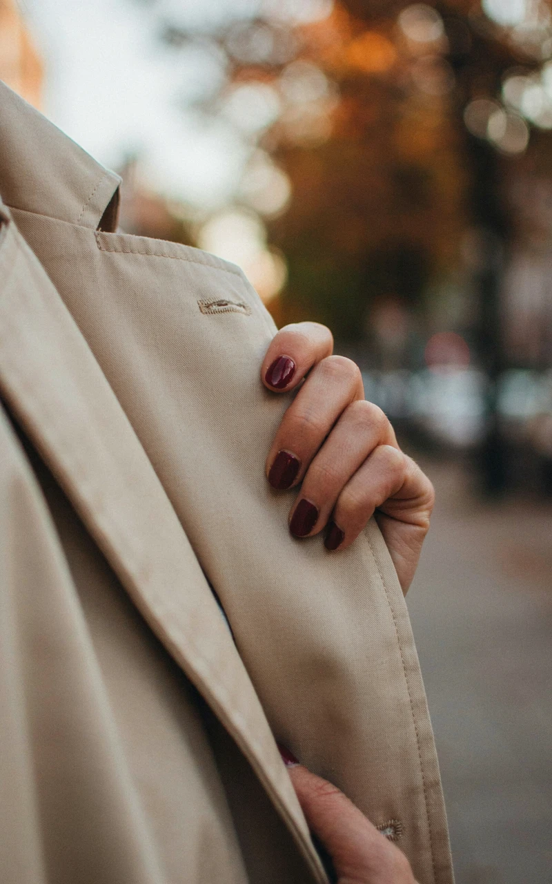 Short glossy deep burgundy nails on a dark brown woman's hand.