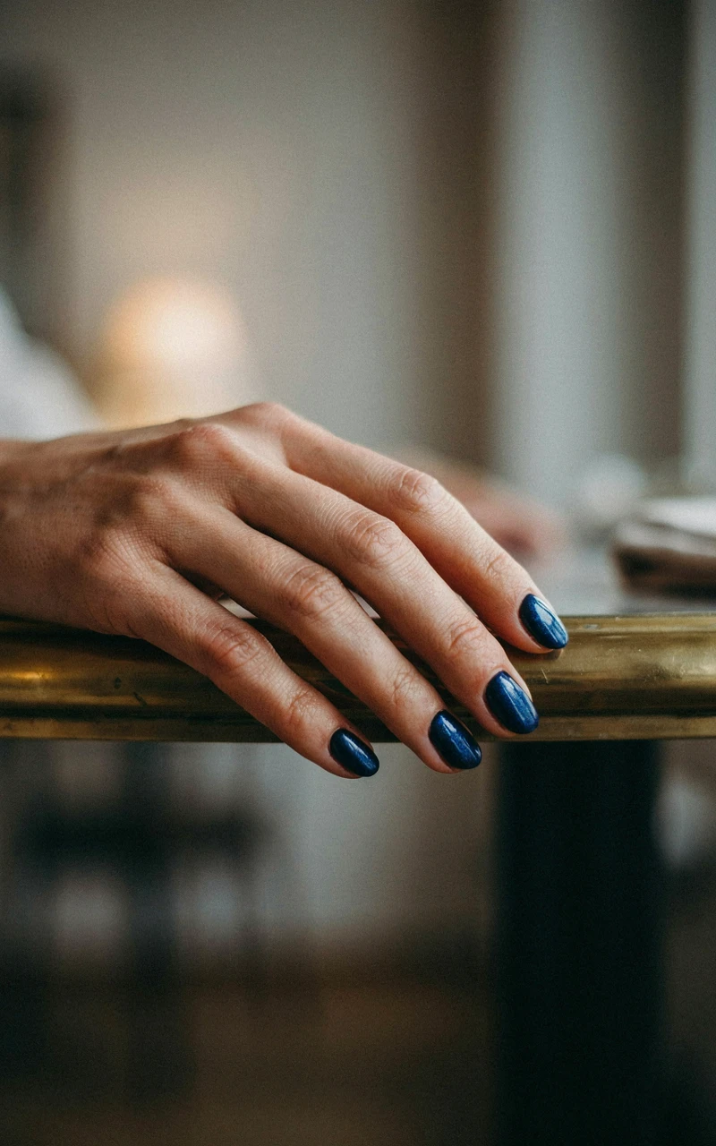 Short shimmering navy blue velvet nails on a dark brown woman's hand.