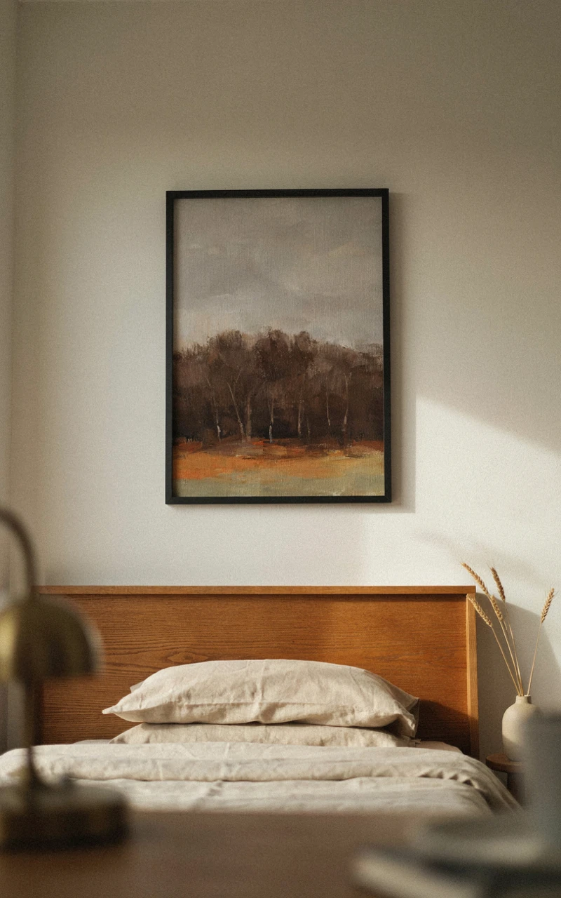 A framed moody autumn landscape print hanging above a wooden headboard.