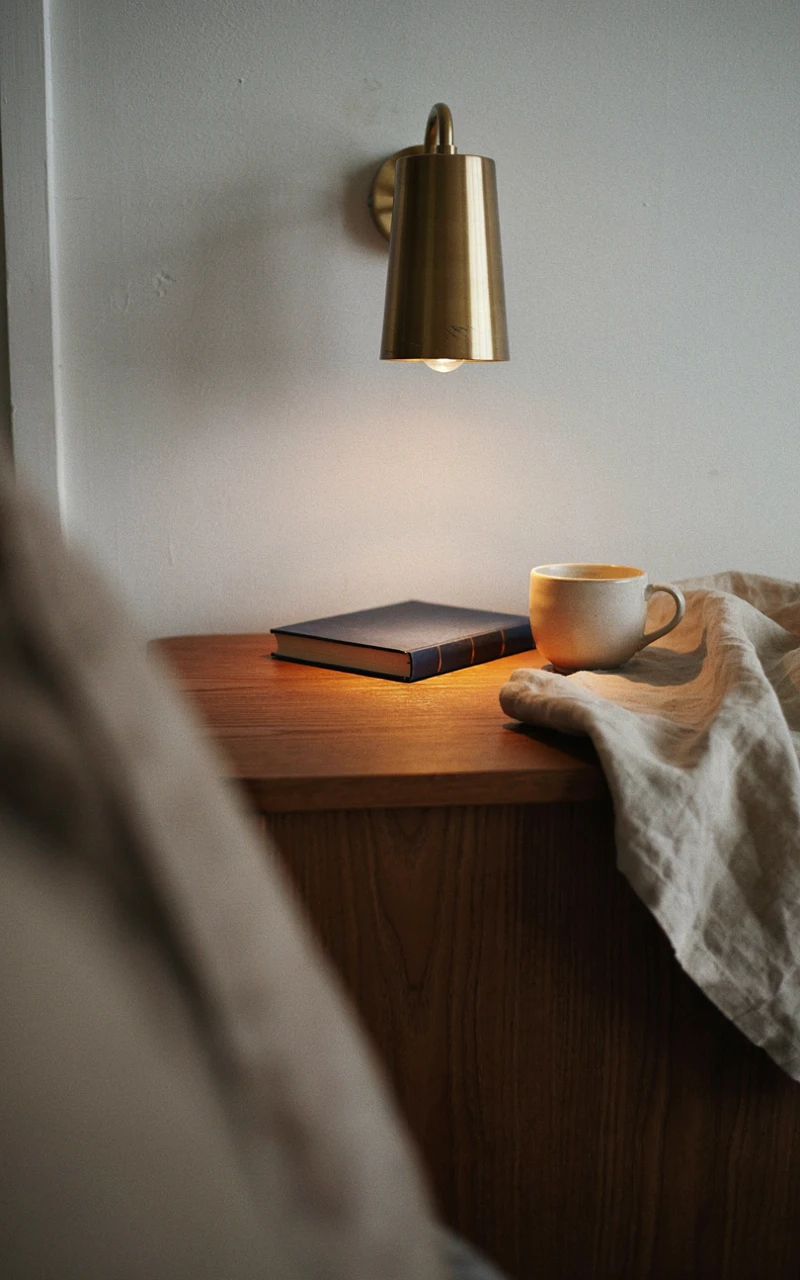 A brushed brass wall sconce mounted above a wooden nightstand.