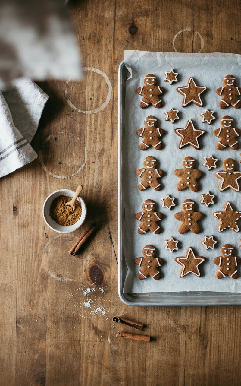 10 Delicious Christmas Dessert Ideas to Start Planning Early 2 Soft gingerbread men and star cookies with white icing on a parchment-lined baking sheet beside cinnamon sticks