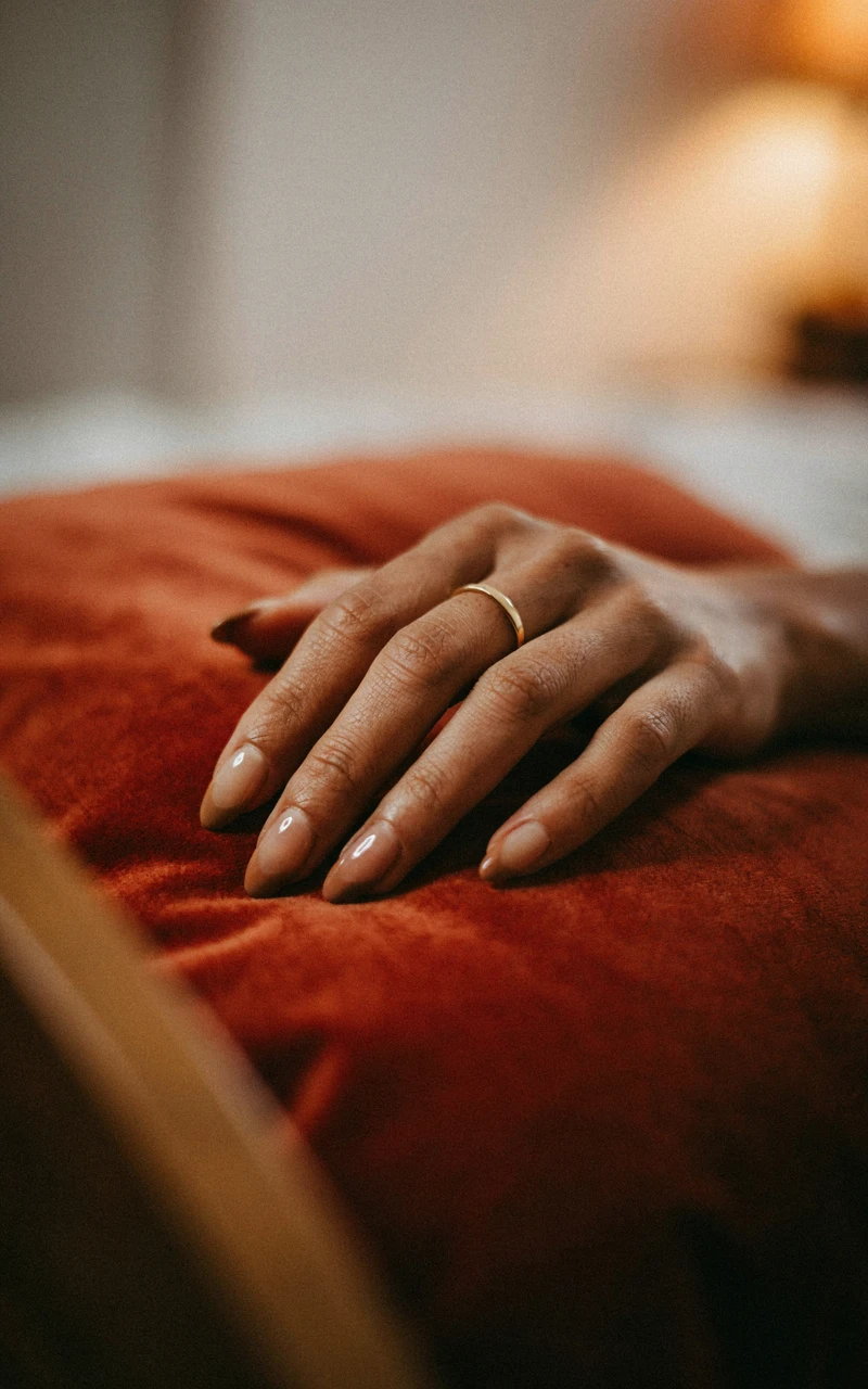 Almond chrome nails fading from beige to mocha brown on a woman's hand resting on a rust velvet pillow