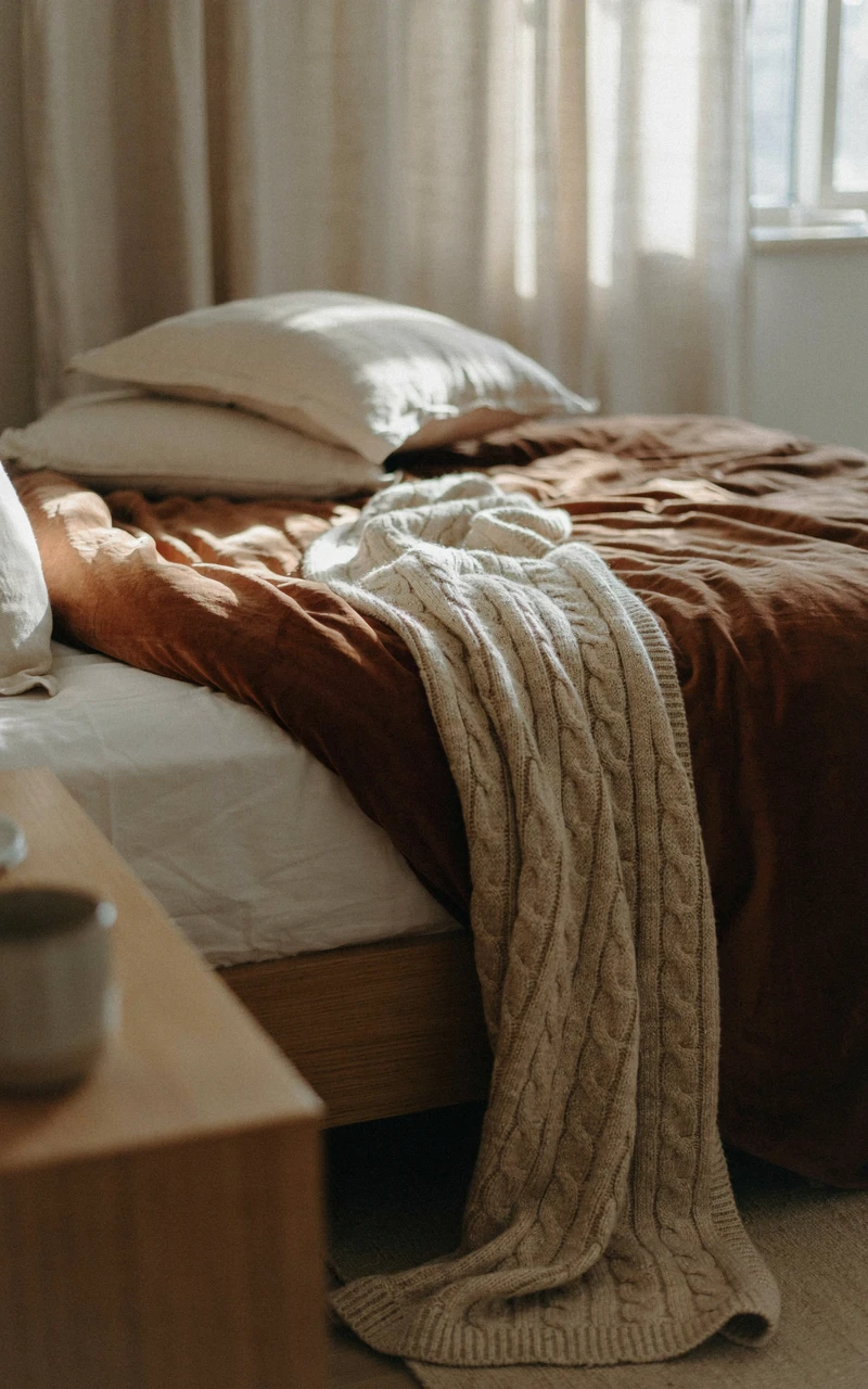 How to Create a Cozy Autumn Bedroom Without Buying Lots of Decor 4 A close-up of a bed layered with white sheets, a brown velvet quilt, and a cream wool throw.
