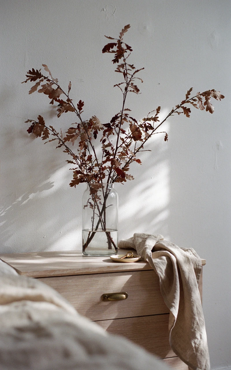 How to Create a Cozy Autumn Bedroom Without Buying Lots of Decor 6 A clear glass vase filled with dried brown and red oak branches sitting on a bedroom dresser.