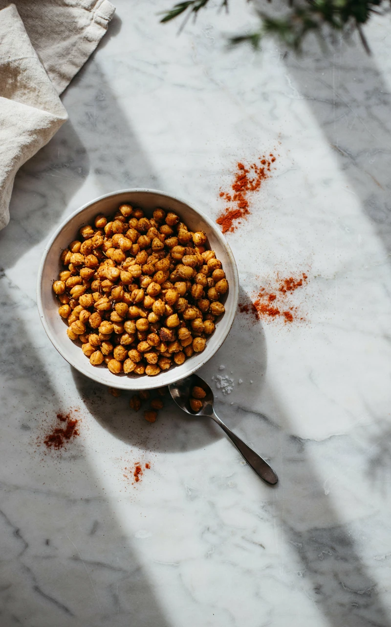 13 Delicious Snack Recipes to Make at Home 2 A white bowl filled with crispy roasted chickpeas seasoned with spices on a marble counter.