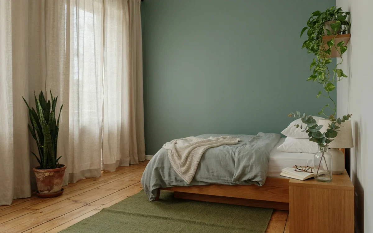 Bedroom showing greenery bedroom ideas: a sage wall, linen bedding, a snake plant, a trailing pothos and eucalyptus in a jar