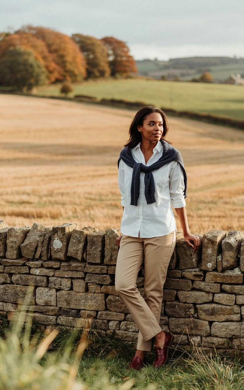 A Woman wearing a navy sweater draped over a crisp white shirt, khaki trousers and burgundy loafers
