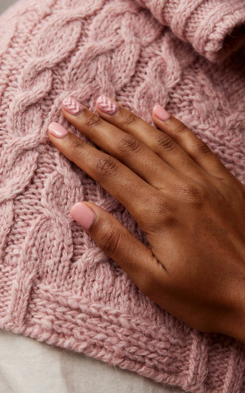A woman's hand on a pink cardigan with matte pink nails and raised cable-knit designs on two accent nails