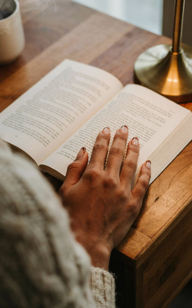 A woman's hand on an open book with sheer pink square nails and thin chocolate brown French tips