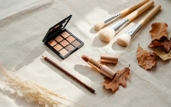 7 Soft Brown Fall Makeup Looks That Feel Warm and Beautiful 23 A flat lay of soft brown fall makeup products including an eyeshadow palette, lipstick, and brushes on a cream linen cloth.